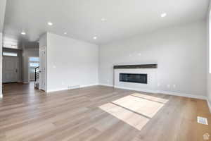 Unfurnished living room with visible vents, a glass covered fireplace, and light wood-type flooring