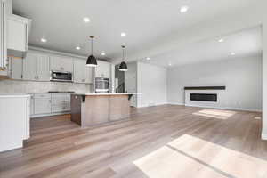 Kitchen featuring recessed lighting, stainless steel microwave, light wood-type flooring, backsplash, and a kitchen island