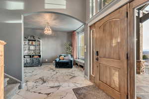 Entryway with a chandelier, baseboards, marble finish floor, stairs, and arched walkways