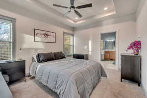 Bedroom with a tray ceiling, light carpet, ensuite bath, baseboards, and recessed lighting