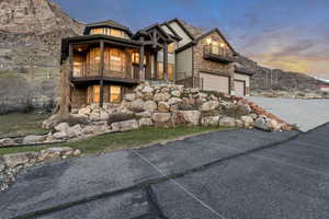 View of front of home with stone siding, driveway, an attached garage, and a balcony