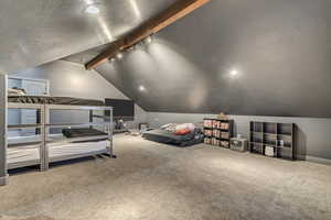 Bedroom featuring vaulted ceiling with beams, track lighting, carpet flooring, and a textured ceiling