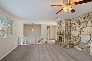 Unfurnished living room featuring a ceiling fan, a stone fireplace, carpet, and baseboards