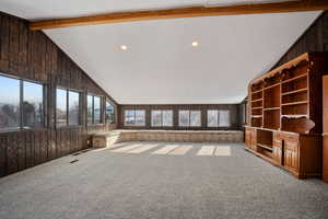 Unfurnished living room featuring recessed lighting, lofted ceiling with beams, wooden walls, and carpet flooring