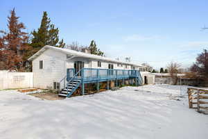 Snow covered house with stairs, fence, a chimney, and a wooden deck