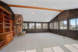 Unfurnished living room with lofted ceiling with beams, wooden walls, and a wealth of natural light