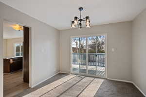 Empty room featuring an inviting chandelier, carpet floors, and baseboards