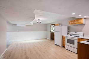 Kitchen with a textured ceiling, a chandelier, white appliances, light wood-type flooring, and brick wall
