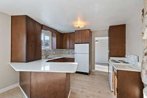 Kitchen featuring light wood-style flooring, a sink, a peninsula, and white appliances