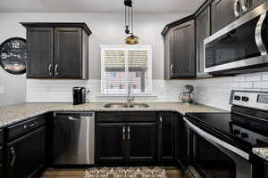 Kitchen featuring a sink, tasteful backsplash, light stone countertops, appliances with stainless steel finishes, and hanging light fixtures