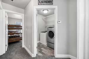 Clothes washing area featuring baseboards, separate washer and dryer, dark colored carpet, and laundry area