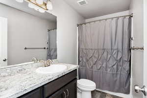 Full bath with curtained shower, visible vents, toilet, and vanity