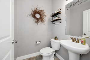 Half bath with toilet, a sink, and baseboards