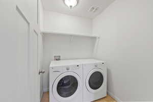 Clothes washing area with laundry area, visible vents, washing machine and dryer, and baseboards