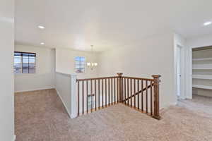Hallway featuring an inviting chandelier, carpet, and an upstairs landing