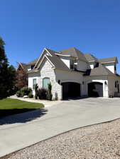 View of property exterior with stone siding, concrete driveway, a garage, and roof with shingles