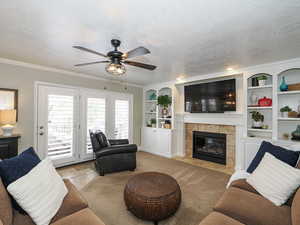 Living area with light colored carpet, a ceiling fan, built in features, and a textured ceiling