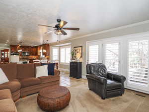 Living room featuring crown molding, a textured ceiling, baseboards, visible vents, and ceiling fan