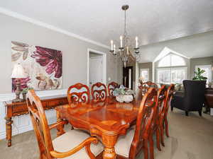 Carpeted dining space featuring ornamental molding, a notable chandelier, lofted ceiling, and a textured ceiling