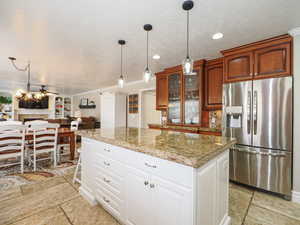 Kitchen with glass insert cabinets, stainless steel refrigerator with ice dispenser, a kitchen island, and stone tile floors