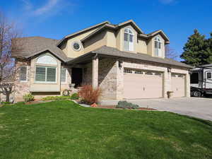 Traditional-style house with a garage, stucco siding, brick siding, a front lawn, and driveway