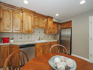 Kitchen with tile counters, brown cabinets, tasteful backsplash, appliances with stainless steel finishes, and a sink
