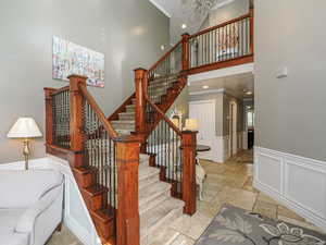 Staircase with stone tile floors, crown molding, a wainscoted wall, a towering ceiling, and a notable chandelier