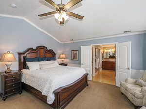 Bedroom with crown molding, vaulted ceiling, ensuite bath, visible vents, and light carpet