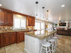 Kitchen featuring stone tile floors, a center island, a breakfast bar, a sink, and a ceiling fan