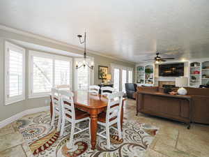 Dining area featuring ornamental molding, ceiling fan with notable chandelier, baseboards, built in shelves, and stone tile flooring