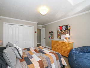 Bedroom with a closet, a textured ceiling, baseboards, and crown molding