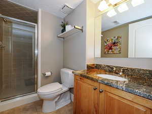 Bathroom featuring a stall shower, tile patterned floors, toilet, vanity, and a textured ceiling