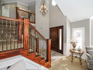 Foyer entrance featuring a wainscoted wall, an inviting chandelier, stairway, and carpet