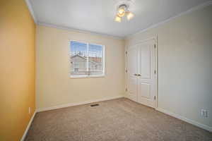 Unfurnished bedroom with a closet, crown molding, carpet flooring, baseboards, and visible vents