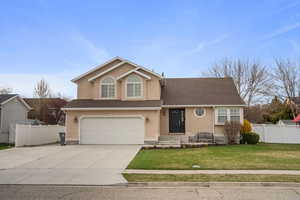 Traditional-style home with driveway, stucco siding, fence, a front lawn, and a garage