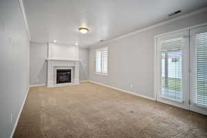 Unfurnished living room featuring ornamental molding, a fireplace with flush hearth, baseboards, and light colored carpet