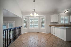 Kitchen with light tile patterned flooring, an inviting chandelier, white cabinetry, a sink, and vaulted ceiling