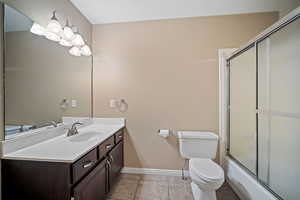 Bathroom with toilet, vanity, tile patterned flooring, baseboards, and shower / bath combination with glass door