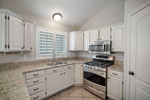 Kitchen with white cabinetry, a sink, stainless steel appliances, and vaulted ceiling