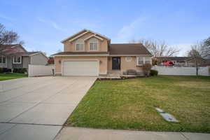 View of front of property featuring driveway, fence, an attached garage, a front yard, and stucco siding