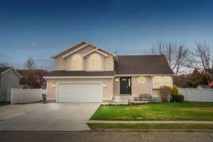 View of front of house with concrete driveway, stucco siding, fence, a garage, and a yard