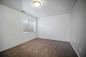 Carpeted spare room with baseboards, a textured ceiling, and visible vents