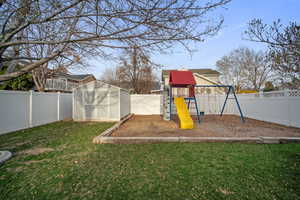 View of playground featuring a fenced backyard, an outbuilding, a yard, and a storage shed