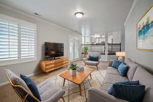 Living area featuring visible vents, baseboards, ornamental molding, light carpet, and a notable chandelier
