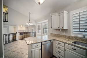 Kitchen featuring white cabinets, a peninsula, a sink, vaulted ceiling, and stainless steel dishwasher
