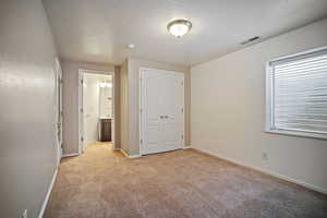 Unfurnished bedroom featuring a closet, a textured ceiling, baseboards, light carpet, and ensuite bath
