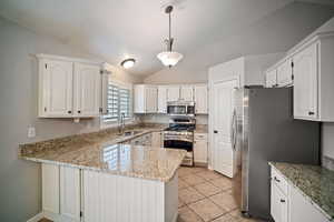 Kitchen with a peninsula, appliances with stainless steel finishes, lofted ceiling, white cabinetry, and a sink