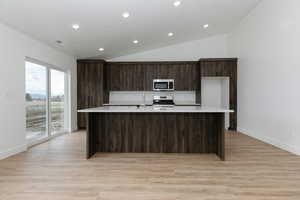 Kitchen with lofted ceiling, light countertops, a large island with sink, and stainless steel appliances