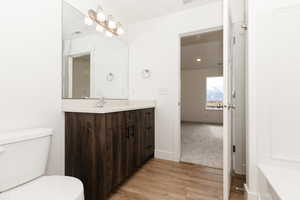 Bathroom with toilet, vanity, wood finished floors, baseboards, and visible vents