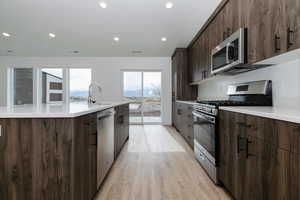 Kitchen featuring light wood finished floors, modern cabinets, a kitchen island with sink, appliances with stainless steel finishes, and a sink